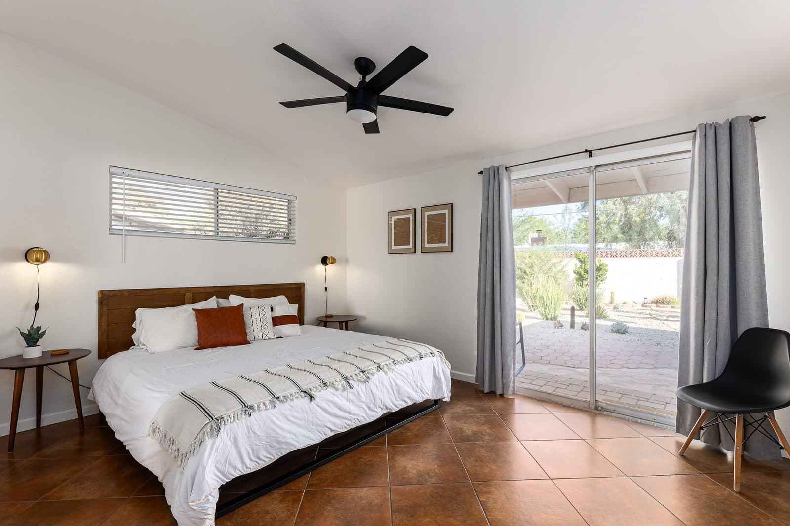King bed in an Airbnb with a white duvet, white pillows, a rust and a patterned decorative pillow, a striped throw, and a low metal frame with a wood headboard