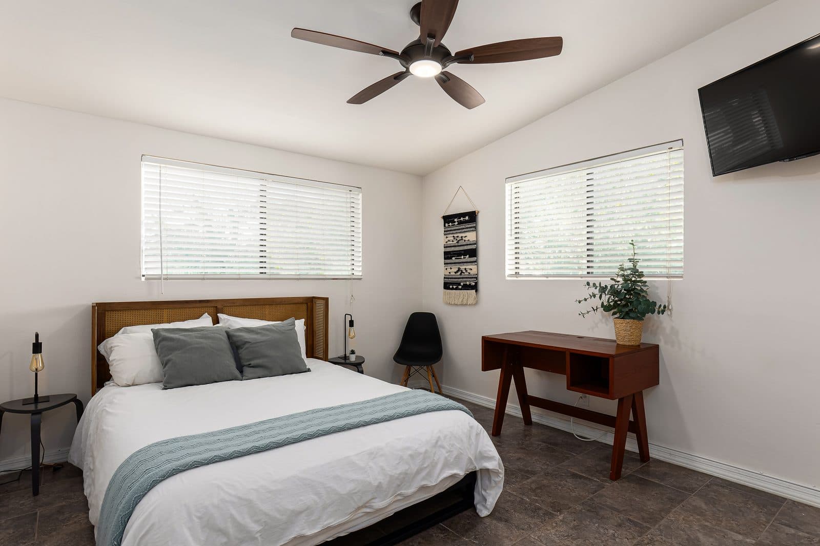 Queen bed in an Airbnb with a white duvet and pillows, two gray decorative pillows and a light blue knit throw, on a metal frame with a cane headboard